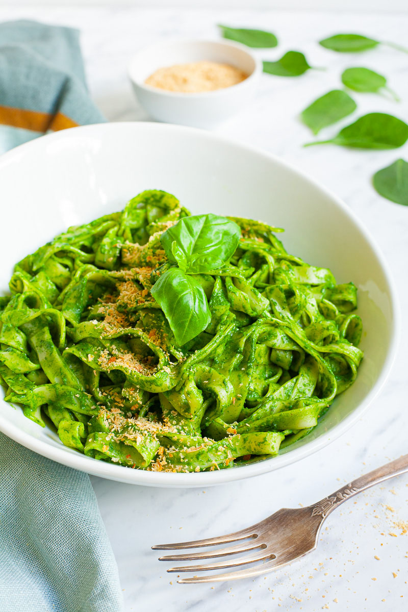 A white bowl full of spinach pasta. 