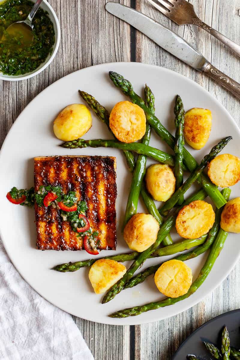 Tofu steak on a plate with potatoes and asparagus.