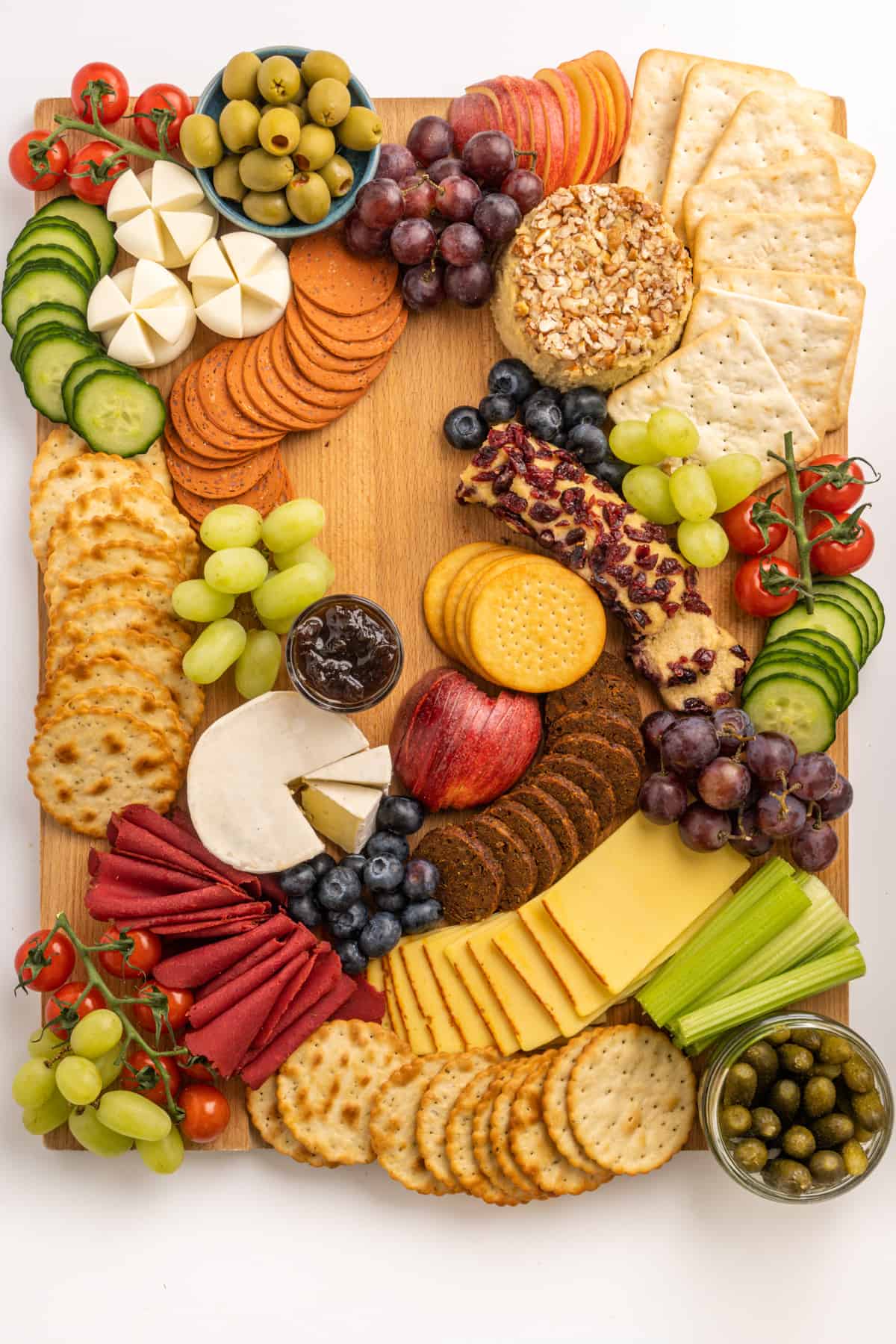 Arranged on a wooden board, various types of crackers, vegan cheeses, ready-to-eat vegan deli slices, fresh fruit and vegetables, olives, pickles and chutney.