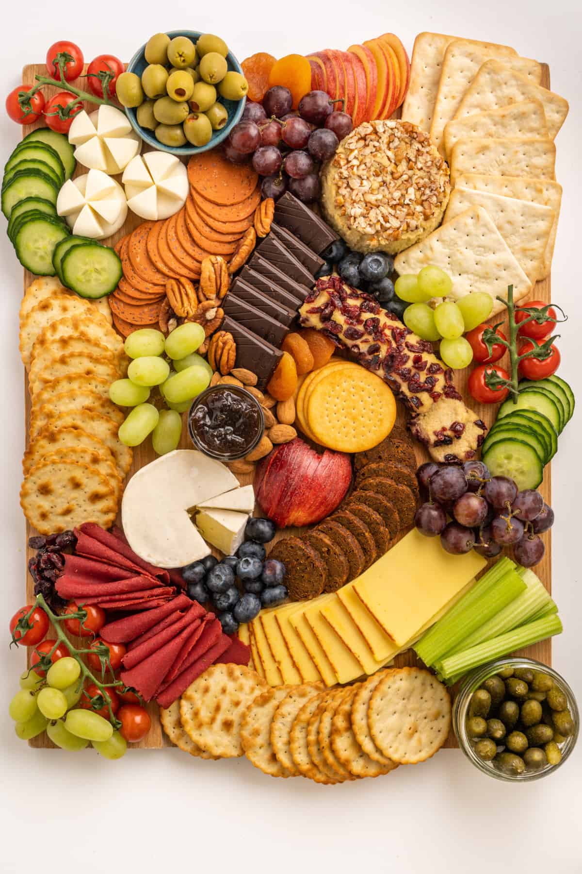 The full charcuterie board consisting of various types of crackers, vegan cheeses, ready-to-eat vegan deli slices, fresh fruit and vegetables, olives, pickles and chutney and topped off with choocolate, nuts and dried fruit.