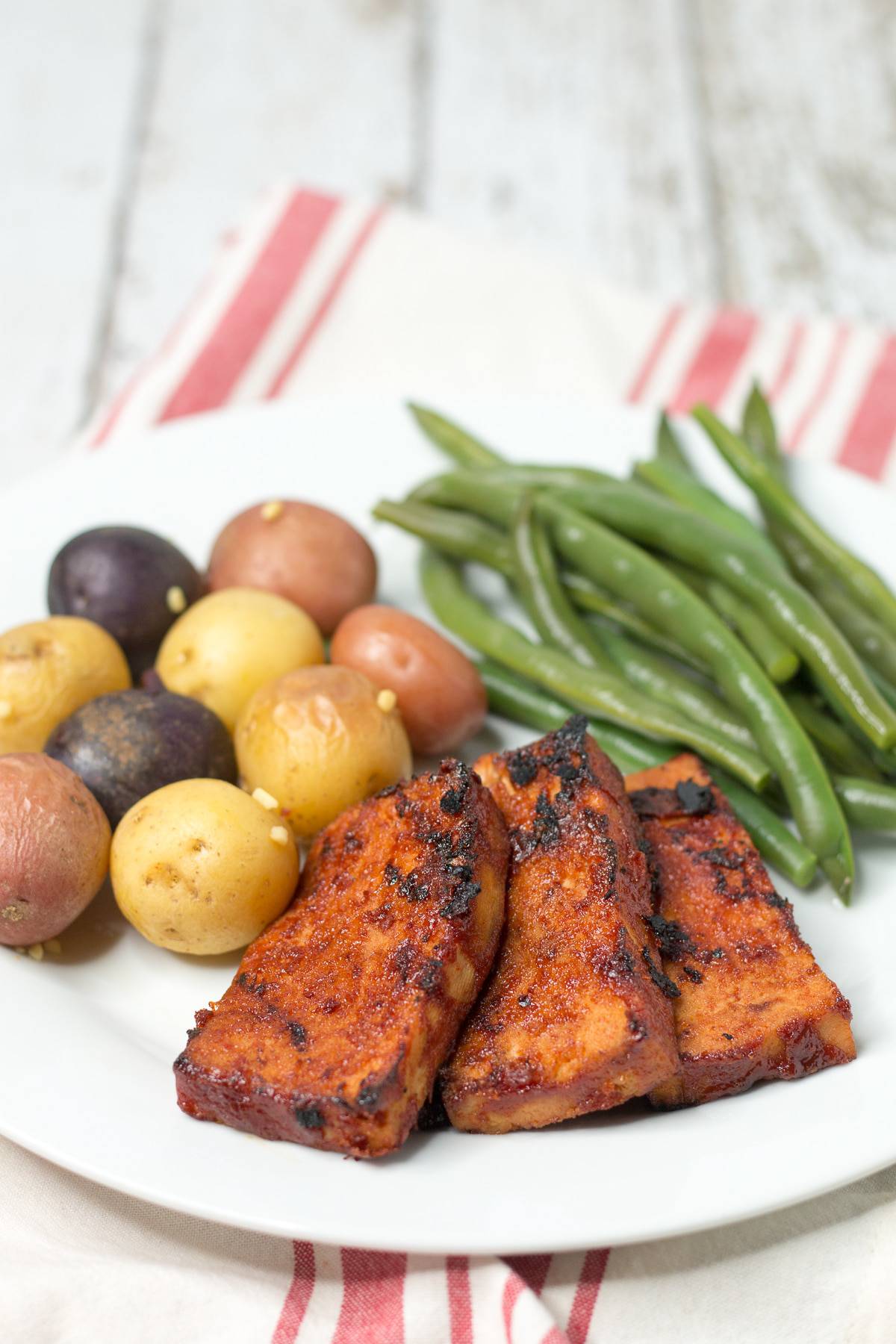 A plate of bbq tofu with potatoes and green beans.