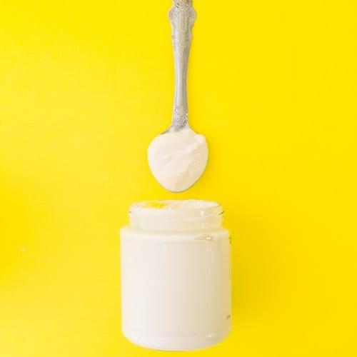 A jar and spoon of vegan mayo on a yellow background.