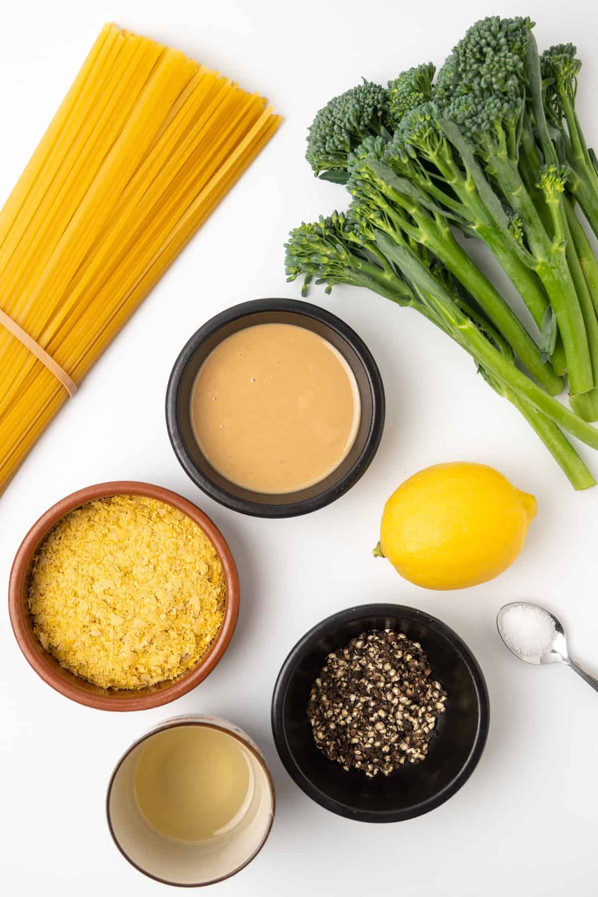 The ingredients of vegan tahini pasta: long shape pasta, tahini, nutritional yeast, olive oil, crushed black pepper, a lemon, salt and some tenderstem broccoli to serve with.