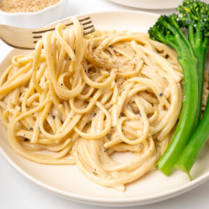 A forkful of pasta is lifted from a plate of pasta in a thick, creamy tahini sauce.