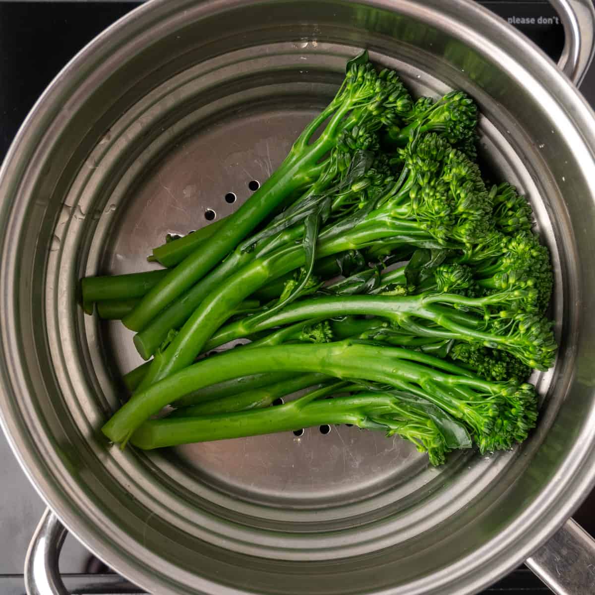 Steamed tenderstem broccoli in a stainless steel steaming insert.
