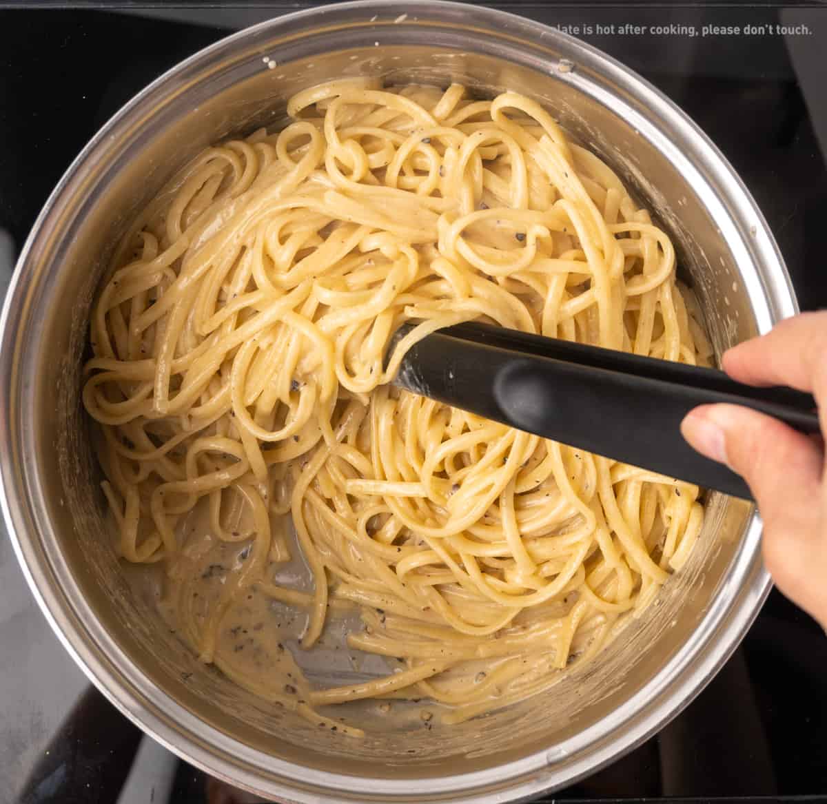 long linguine pasta stirred into a glossy, light brown creamy sauce in a saucepan.