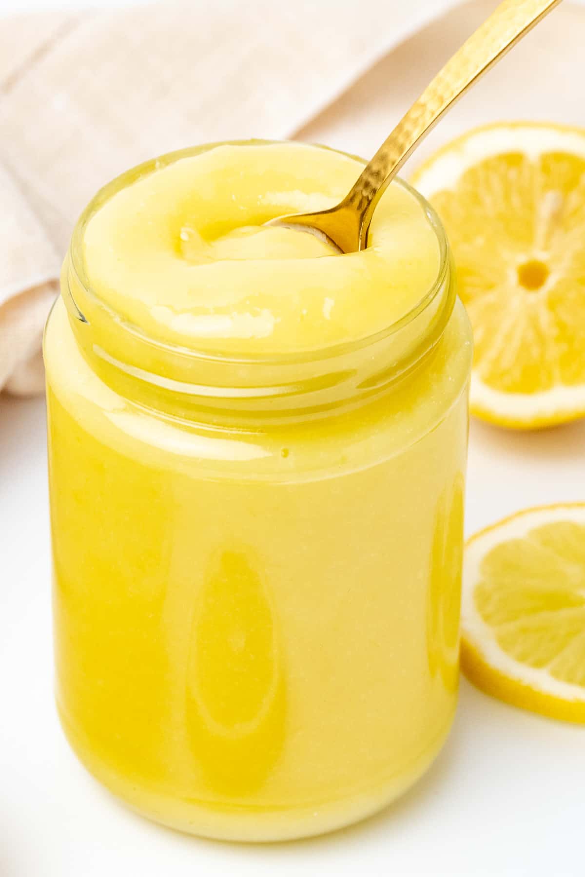 Ένα χρυσό κουταλάκι του γλυκού βυθίζεται σε ένα βάζο με λείο, παχύρρευστο και κρεμώδες τυρόπηγμα λεμονιού.