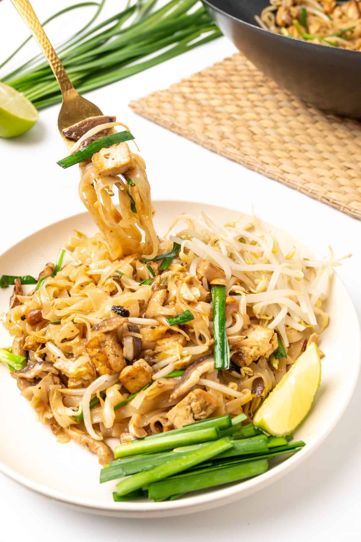 A fork digs into a plate of pad thai noodles.