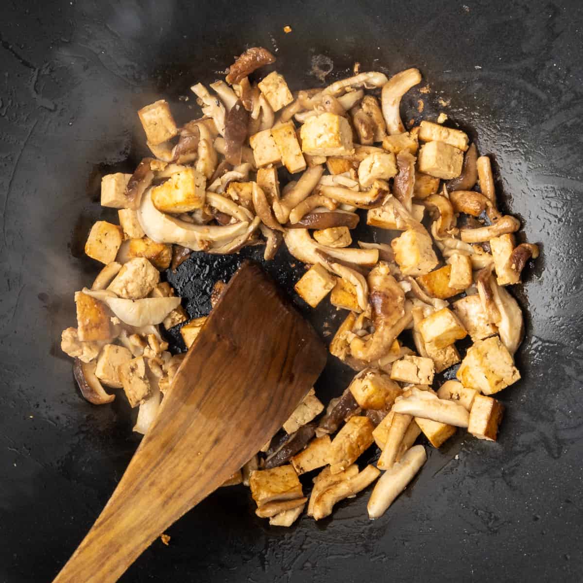 Stir-frying tofu and shiitakes mushrooms in a wok.