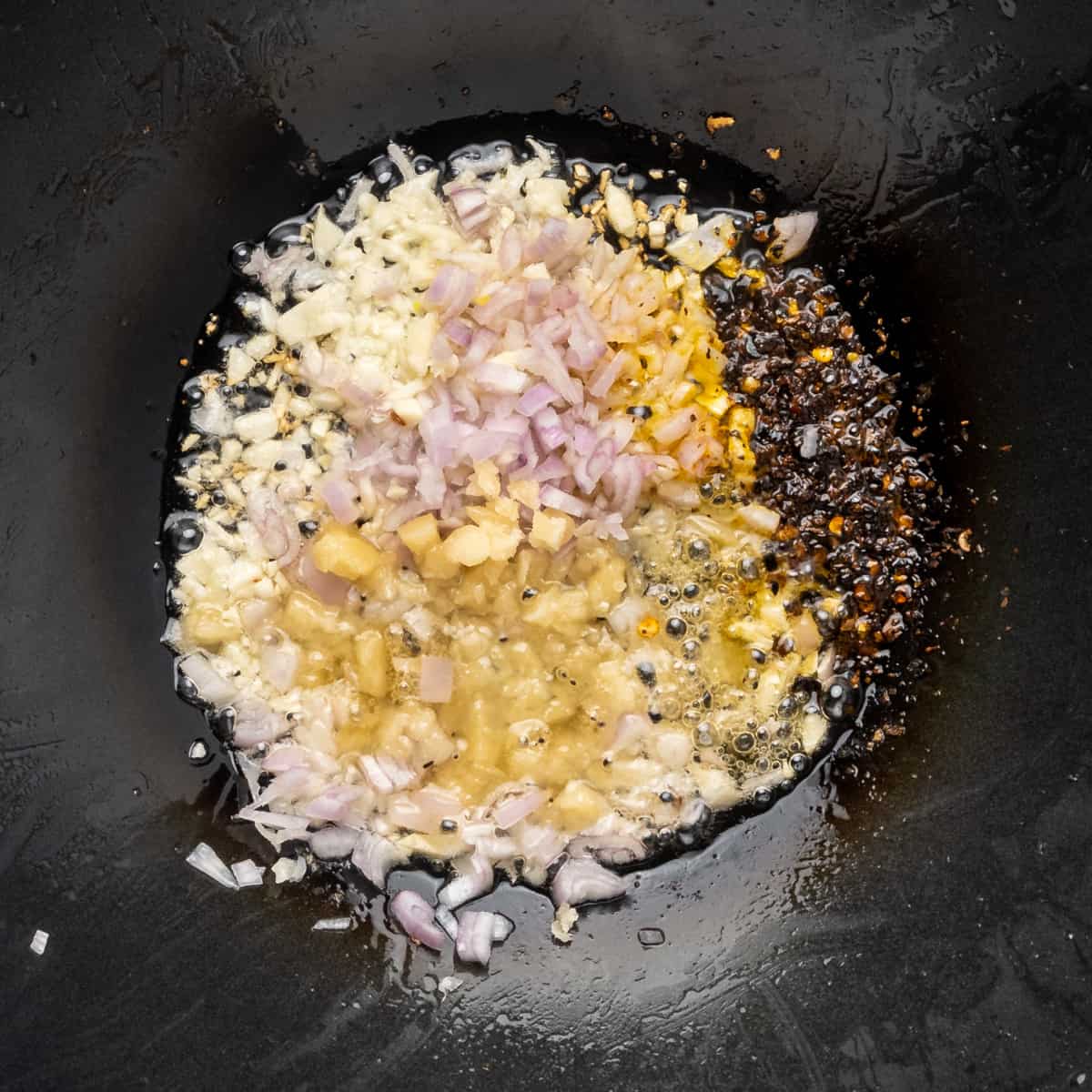 Shallots, garlic, palm sugar and chilli flakes frying in oil.