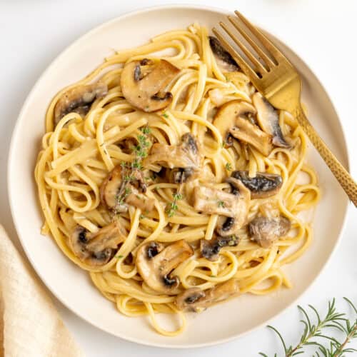 A plate of creamy mushroom pasta garnished with sprigs of fresh thyme.