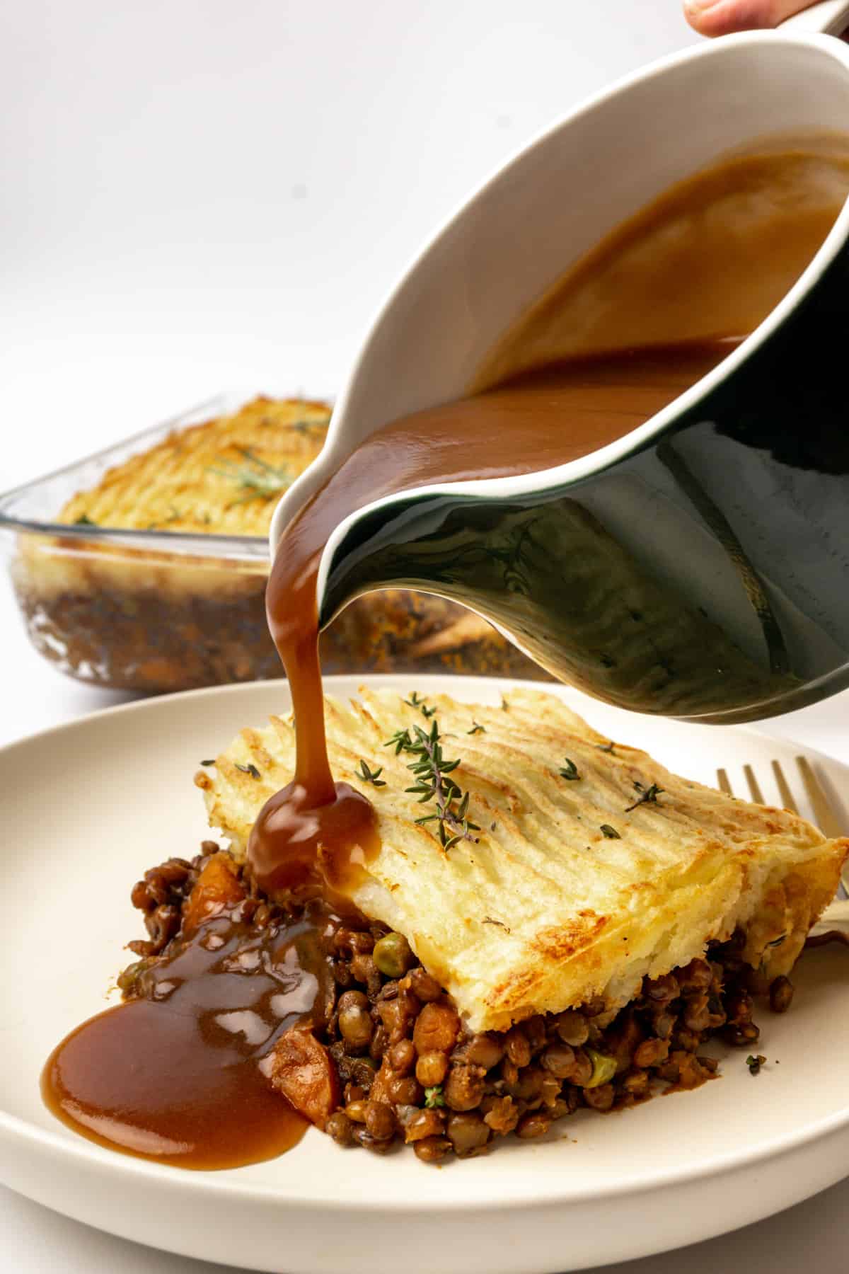 Gravy poured from a gravy jug onto a plate of shepherd's pie.