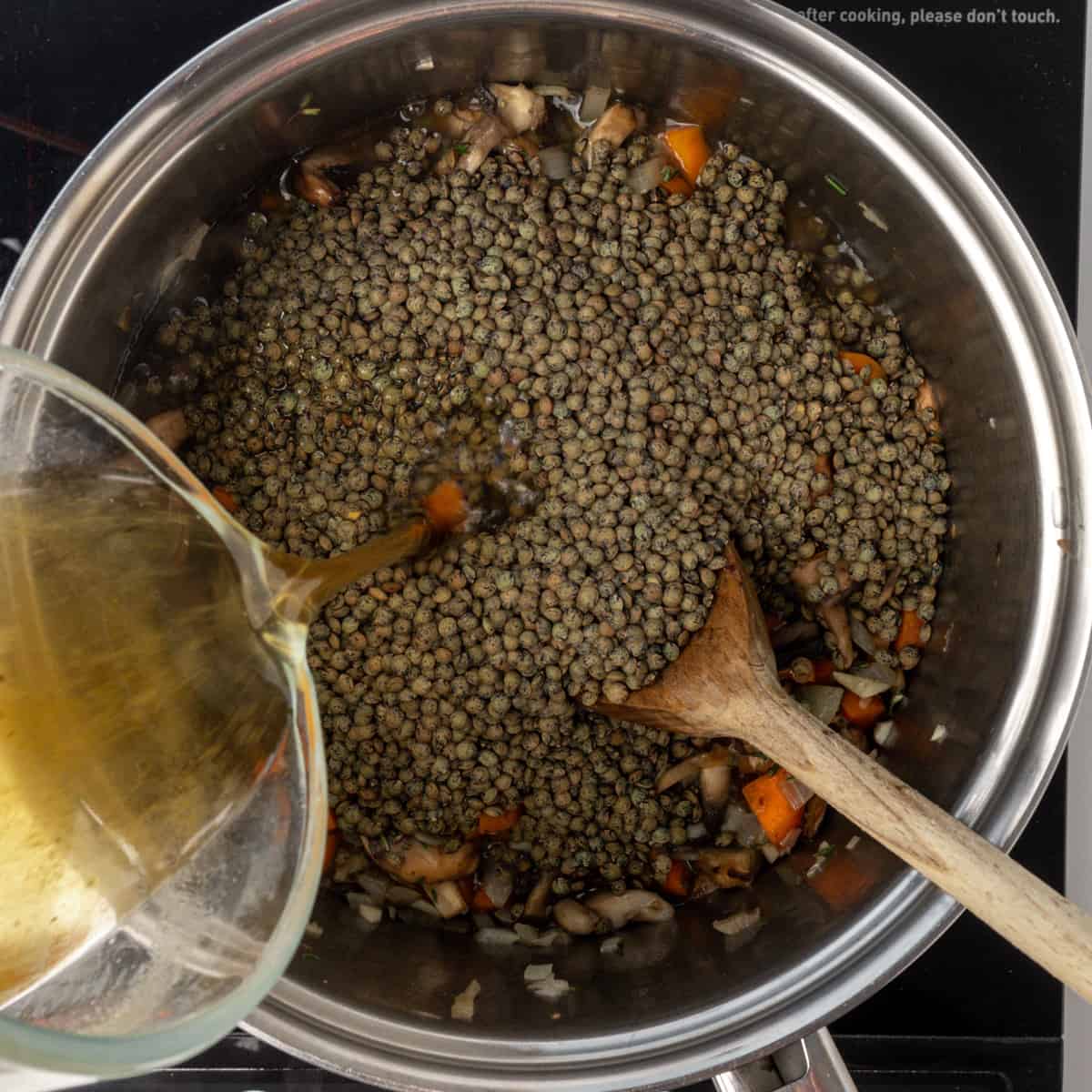 Lentils and vegetable stock added to vegetables in a large saucepan.