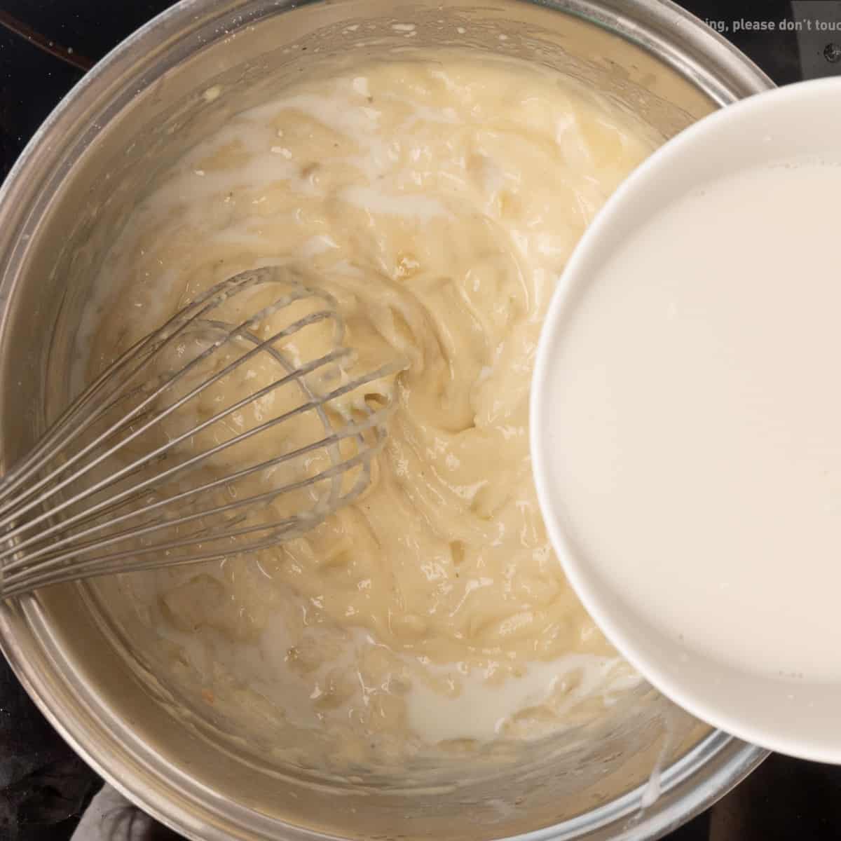 A whisk stirring almond milk into a thick creamy sauce.