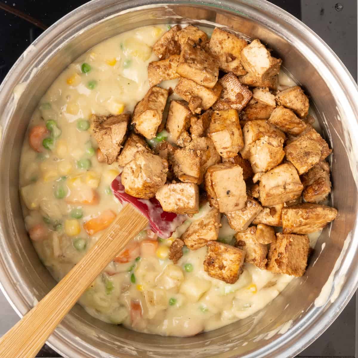 Tofu cubes being added to the creamy vegetable filling for vegan pot pie.