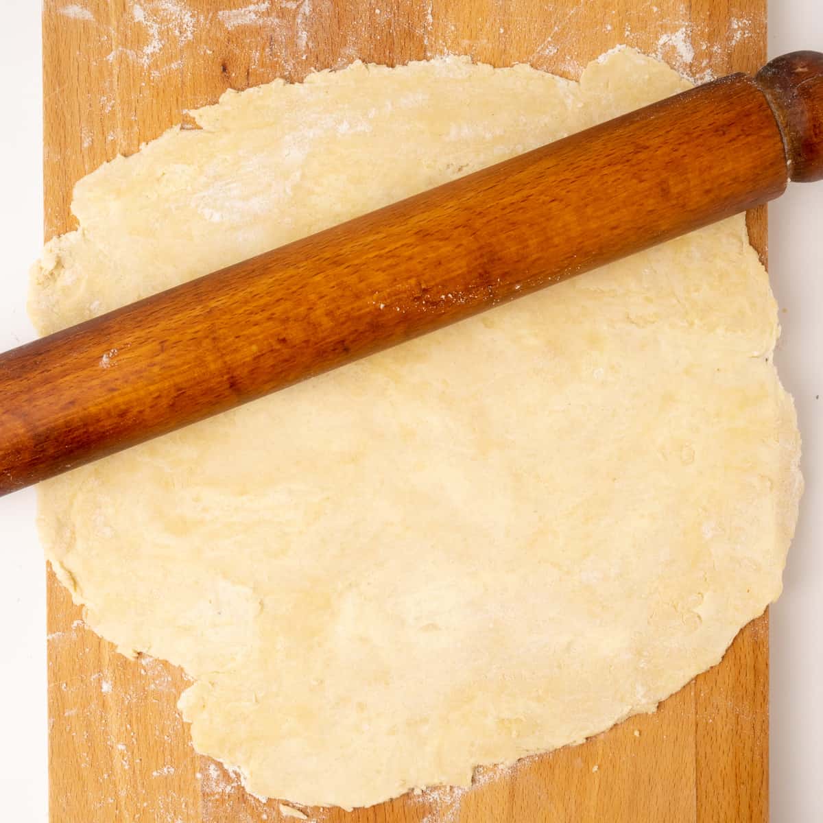 Pastry rolled out with a rolling pin on a wooden board.