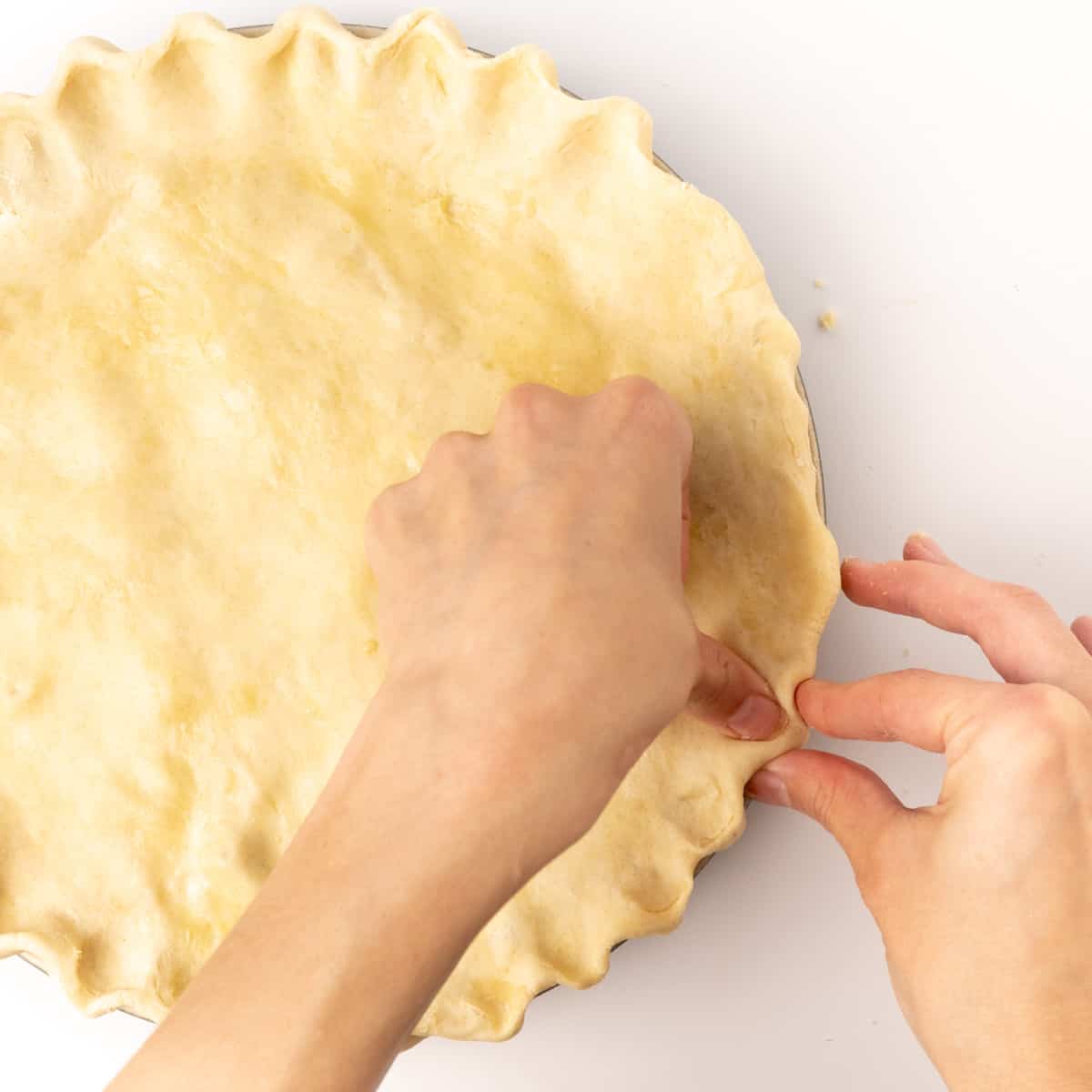 Two hands crimping and fluting the edges of a pie.