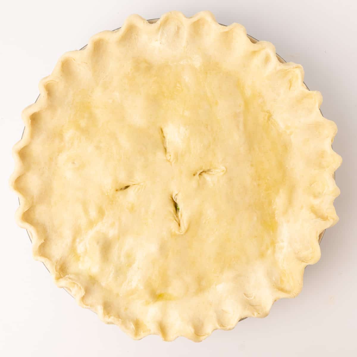 A pie before being cooked, with fluted edges and four incisions in the top.