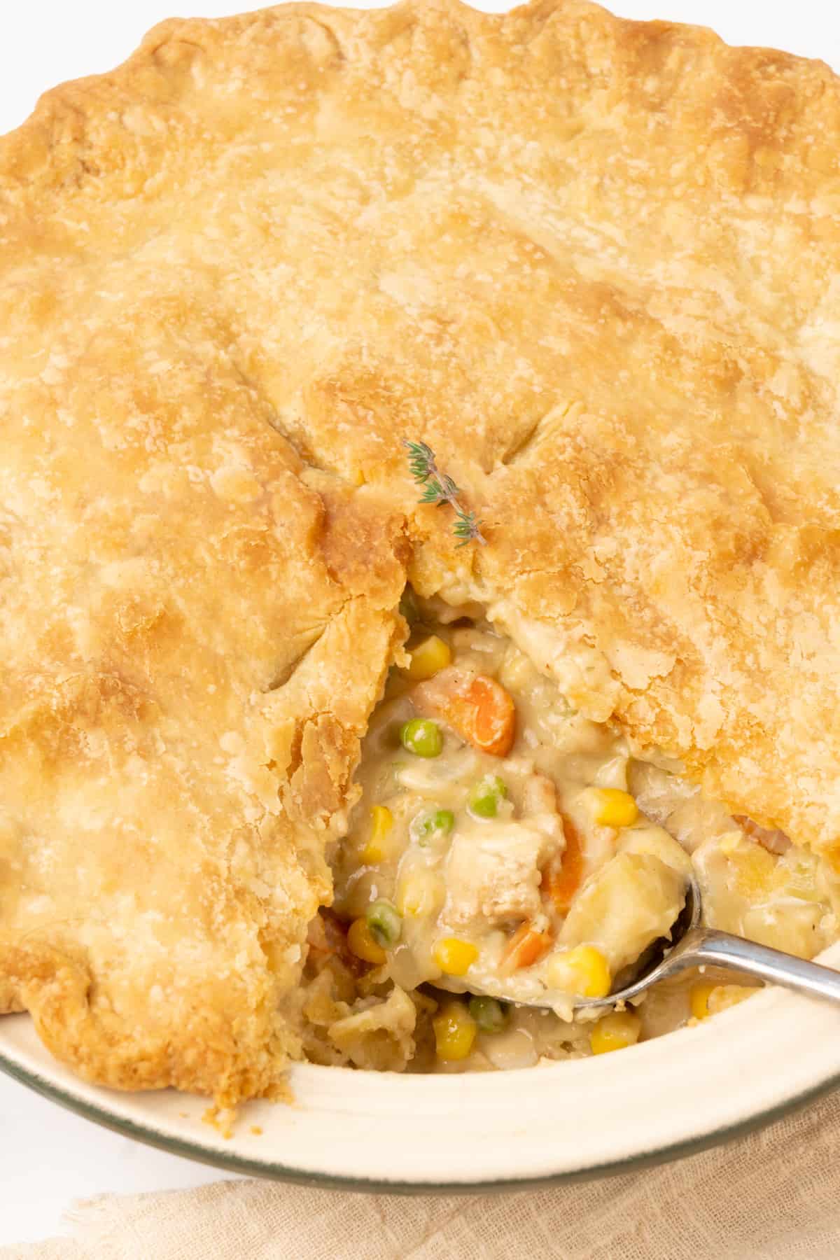 A cut vegan pot pie in a dish, with a slice removed and a serving spoon full of filling.