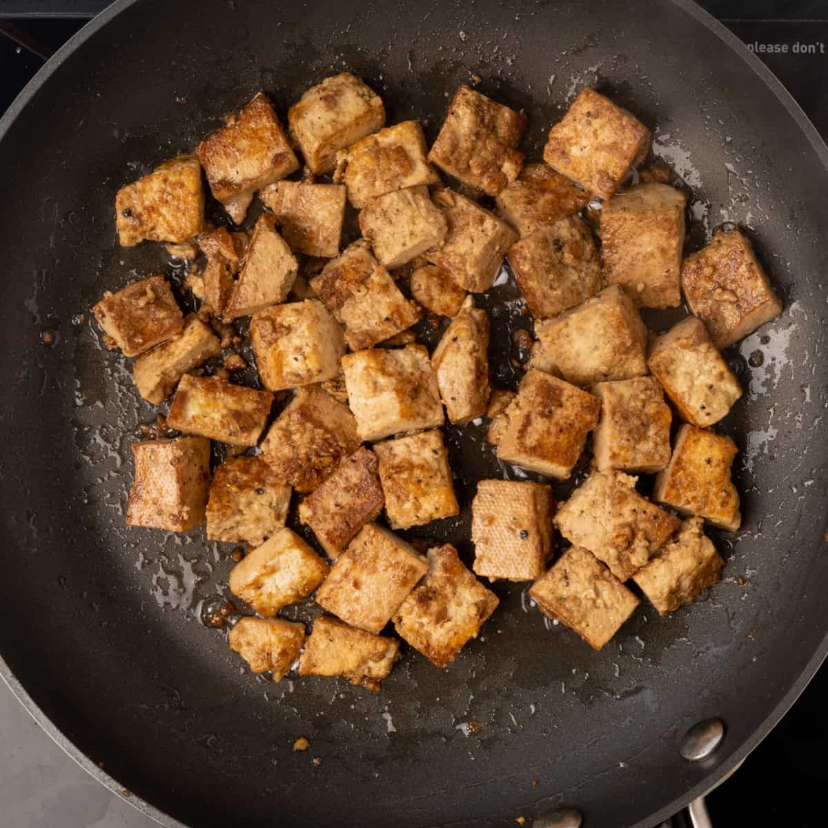 Tofu being fried golden brown in a frying pan.