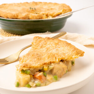 A slice of vegan pot pie on a plate, displaying the creamy filling full of tofu pieces and vegetables.