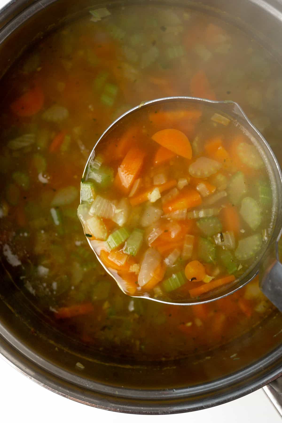 A ladle of broth with pieces of carrots and celery.