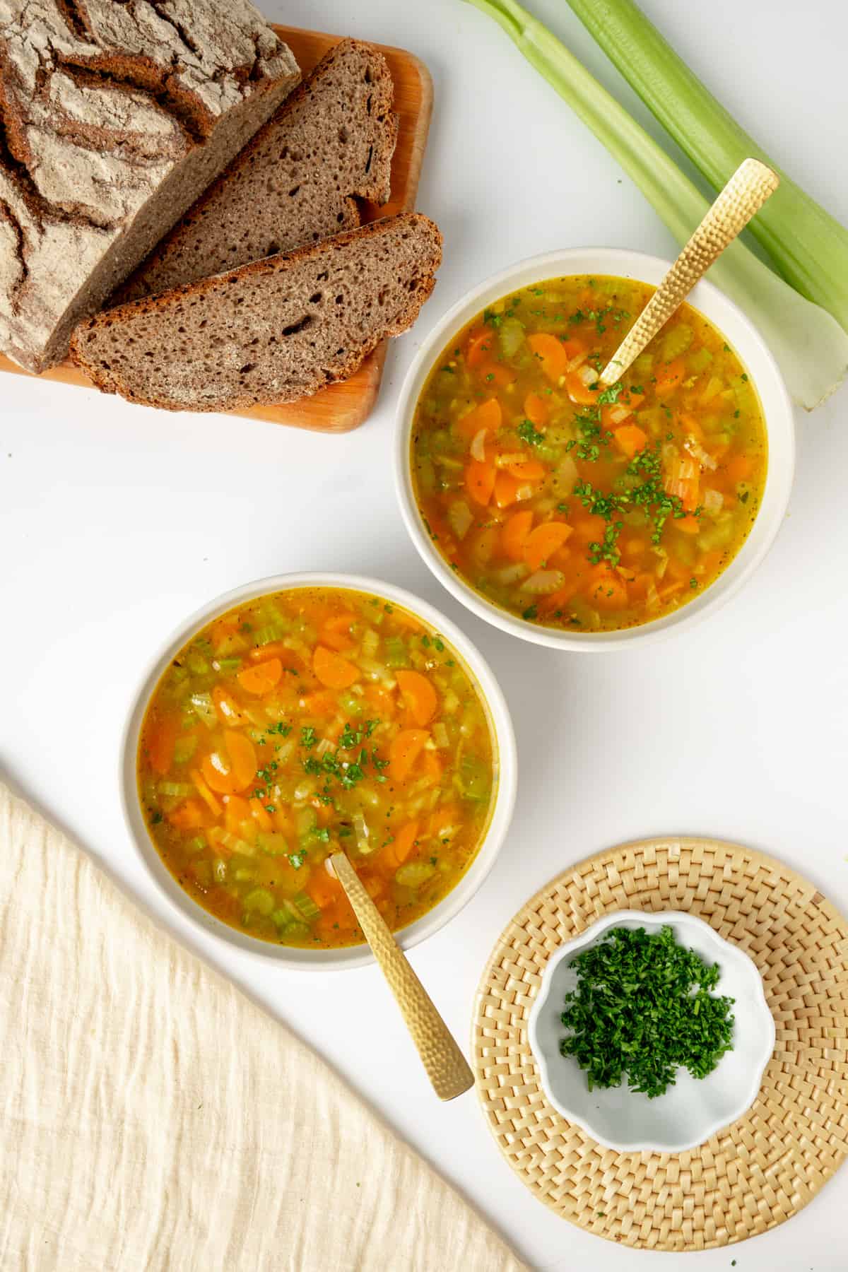 Two bowls of carrot and celery soup served with bread and chopped parsley.