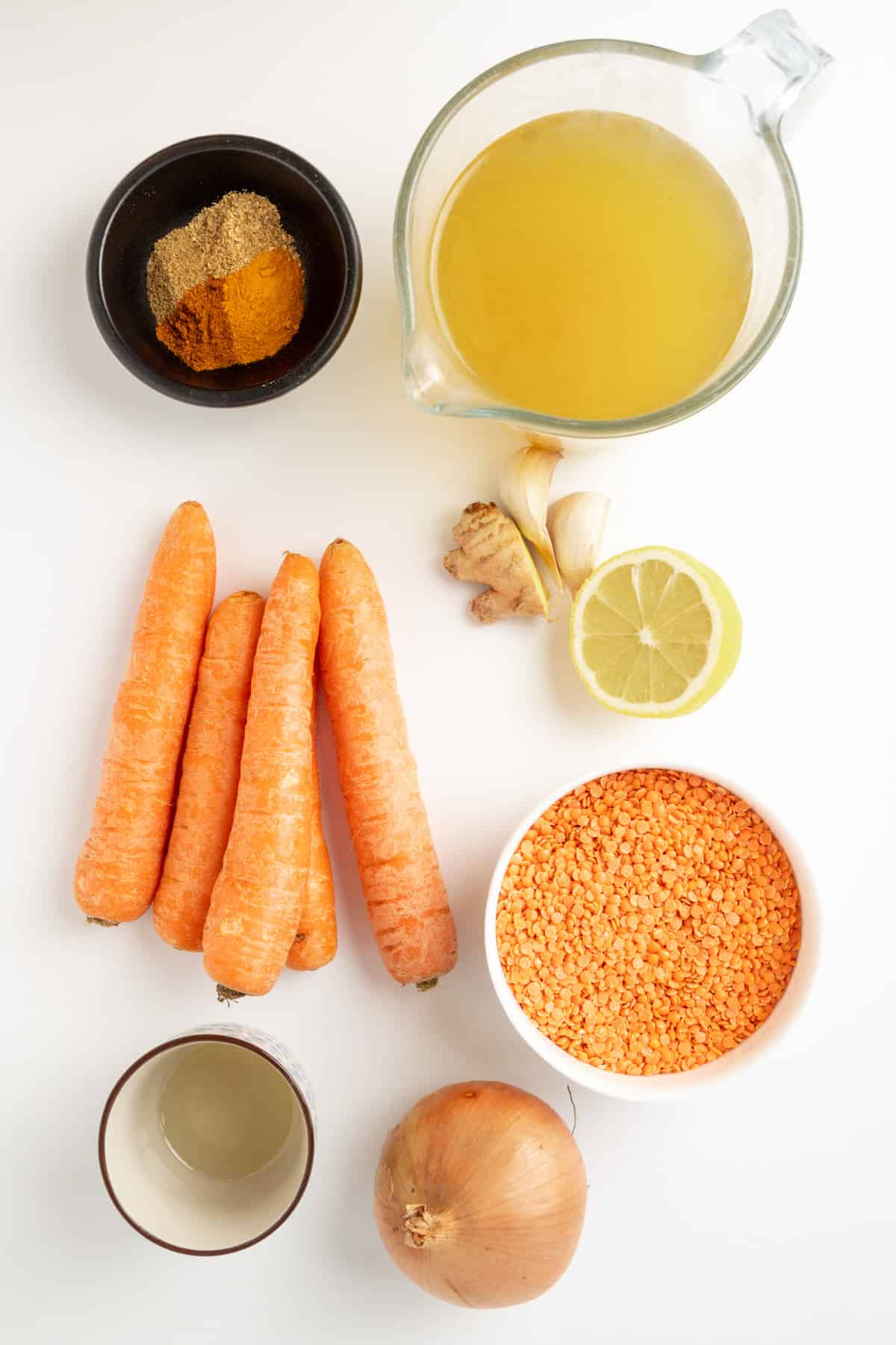 Ingredients for carrot and lentil soup laid out on a white surface.