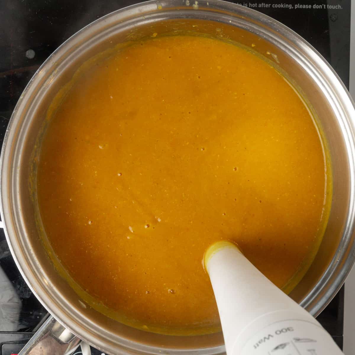 An immersion blender liquidizing a smooth orange coloured soup in a saucepan.