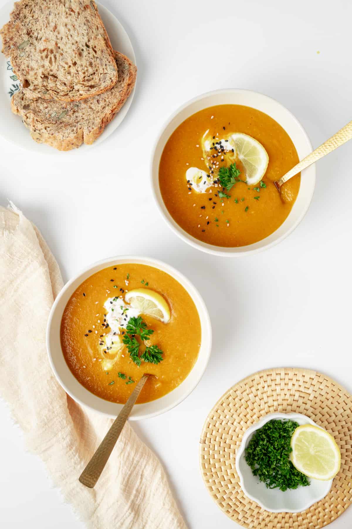 Two bowls of blended carrot and lentil soup served with bread.
