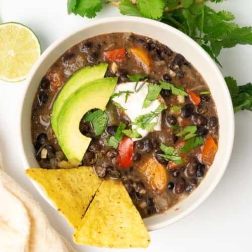 A portion of vegan black bean soup garnished with yogurt, slice of acocado and chopped corainder leaves.