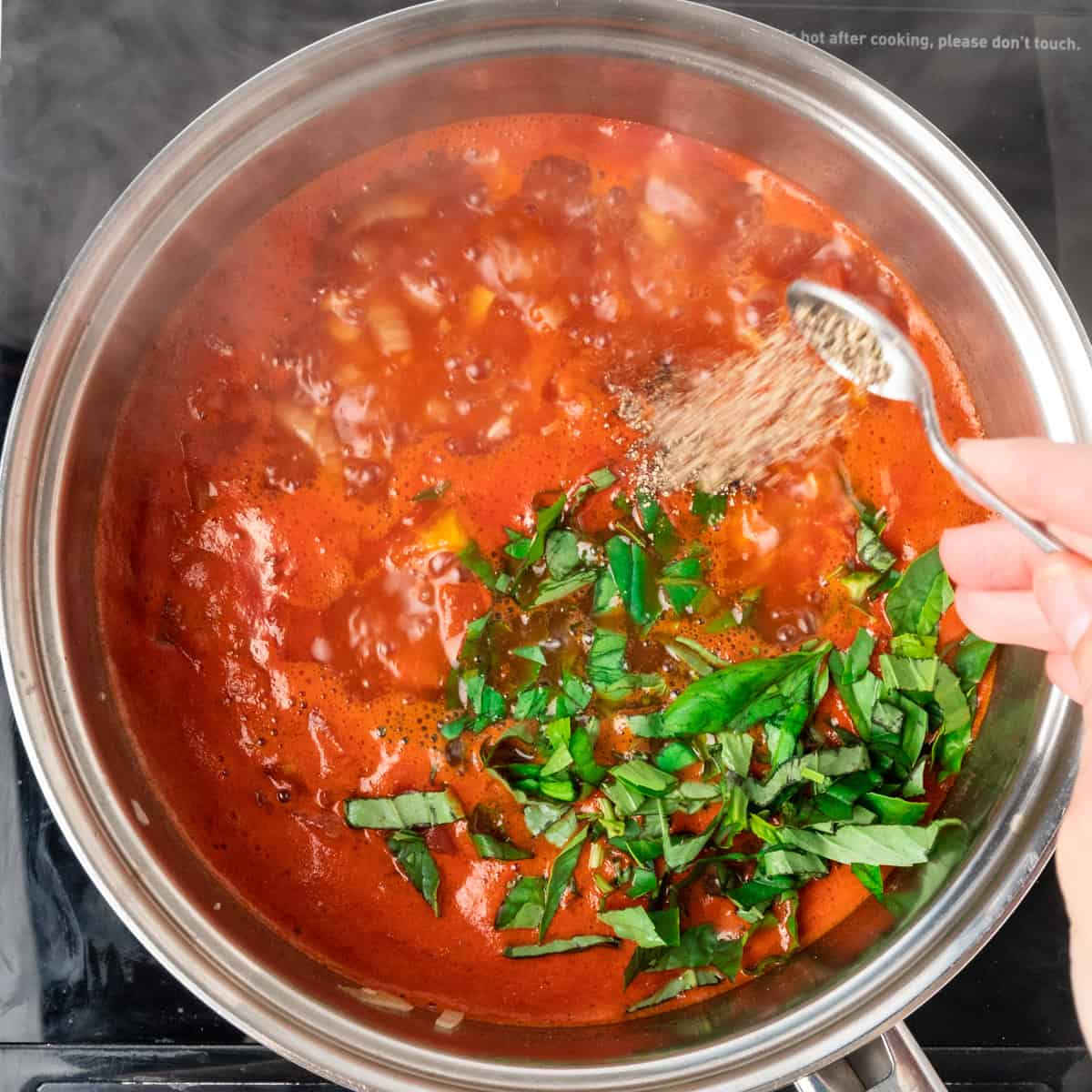 Adding basil and black pepper to simmering tomatoes.