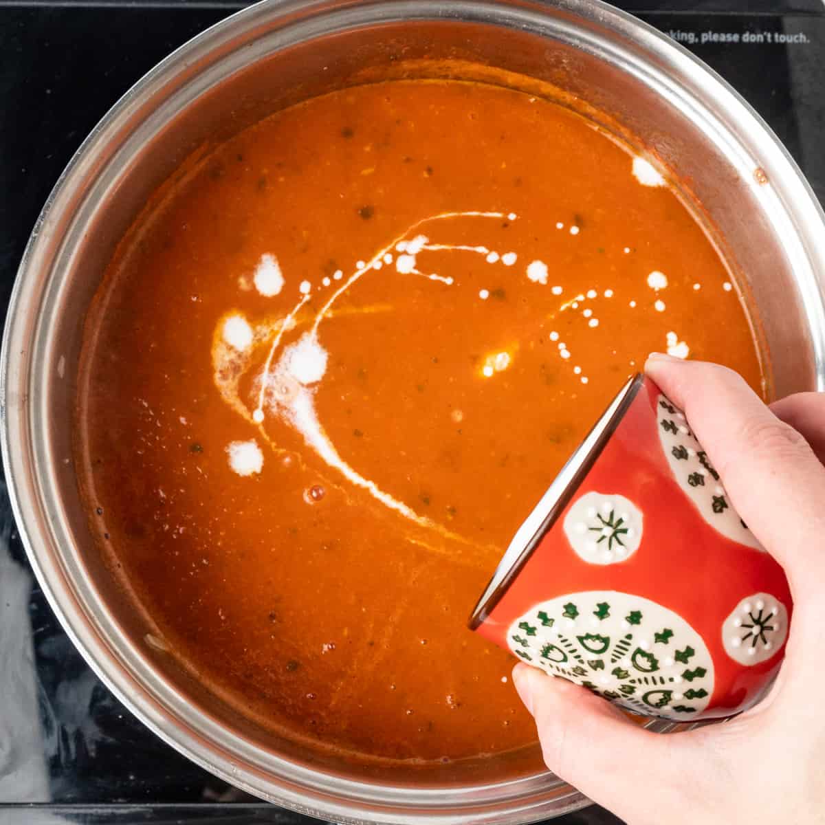 Drizzling vegan cream into a pot of tomato soup.
