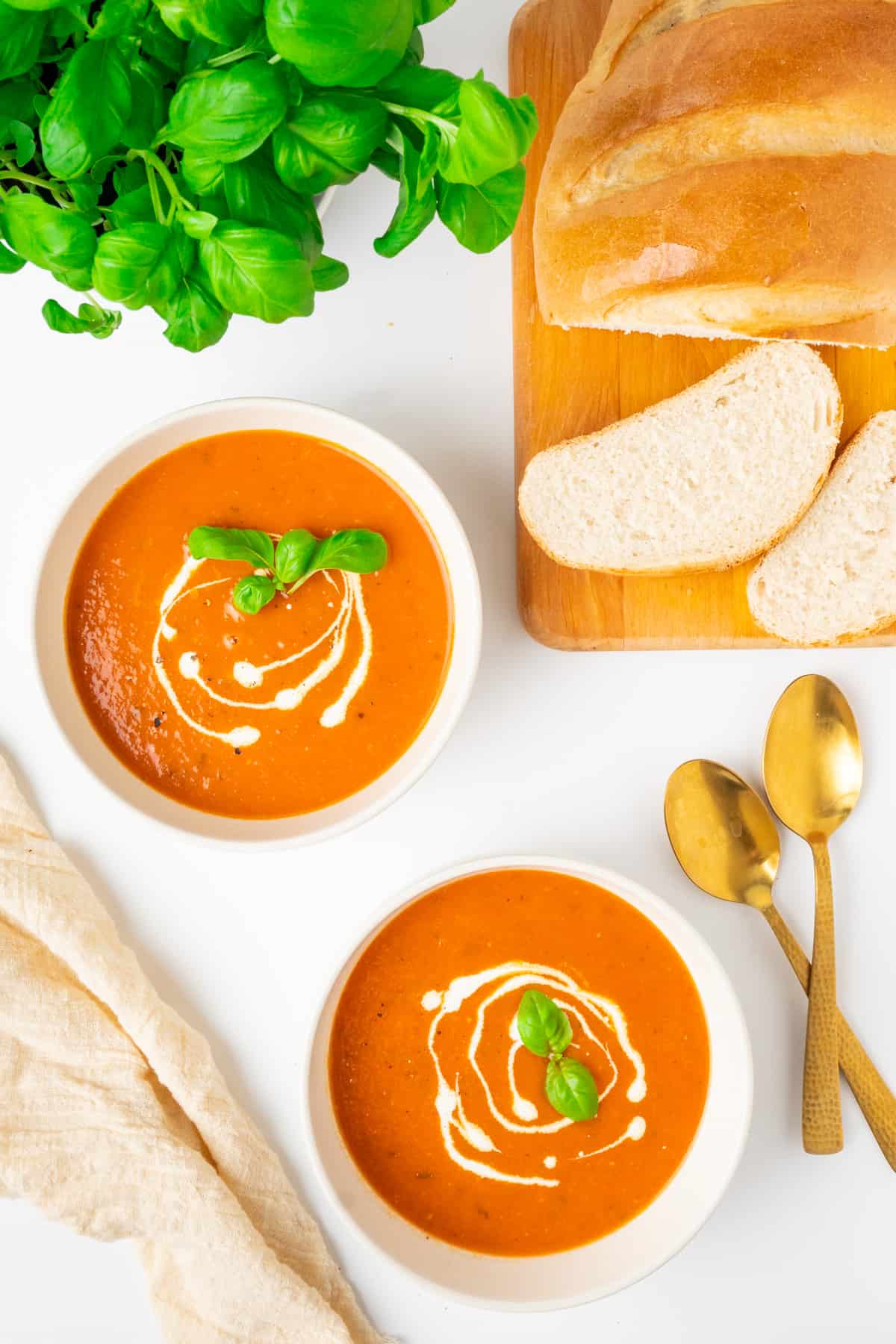 Two bowls of tomato soup next bread and a pot of basil.