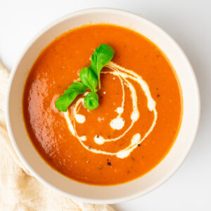 A bowl of tomato soup garnished with a drizzle of vegan cream and basil leaves.