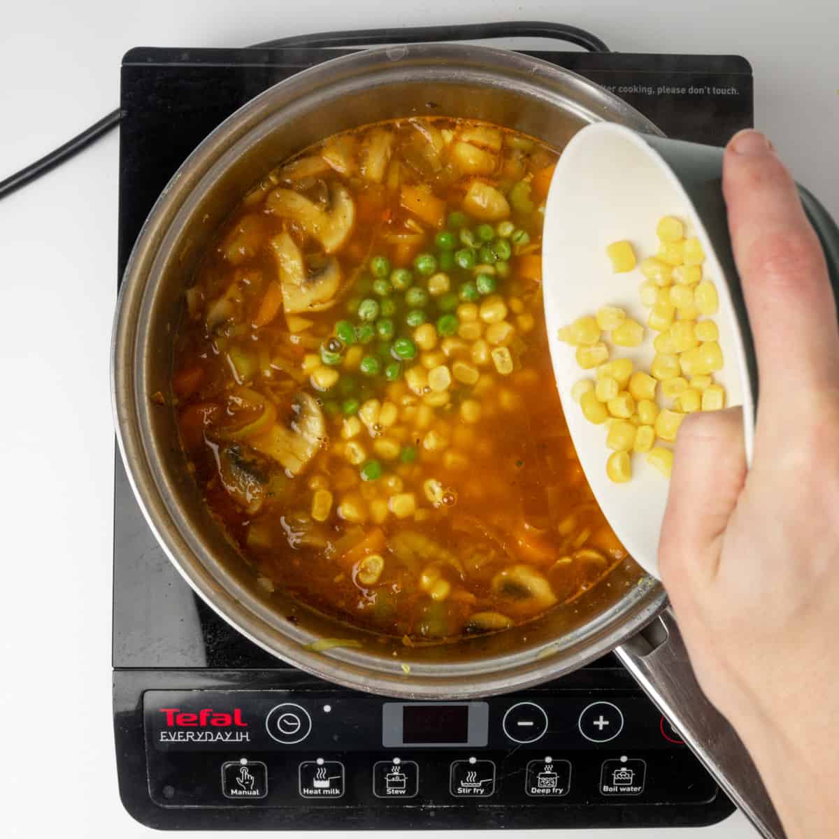 Adding vegetable stock, peas and sweetcorn to veggies in a pan.