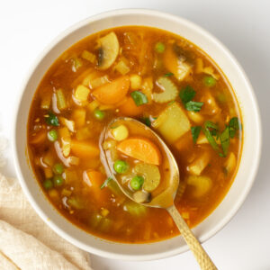 A spoon scoops up some celery, carrot, corn and peas from a bowl of vegetable soup.