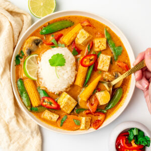 A hand lifts a spoonful of Thai curry.