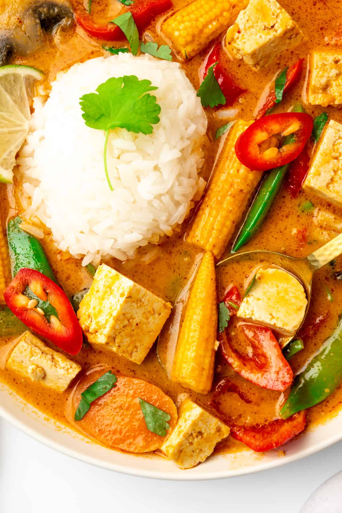 A spoon scoop ups some veggies from a bowl of curry.