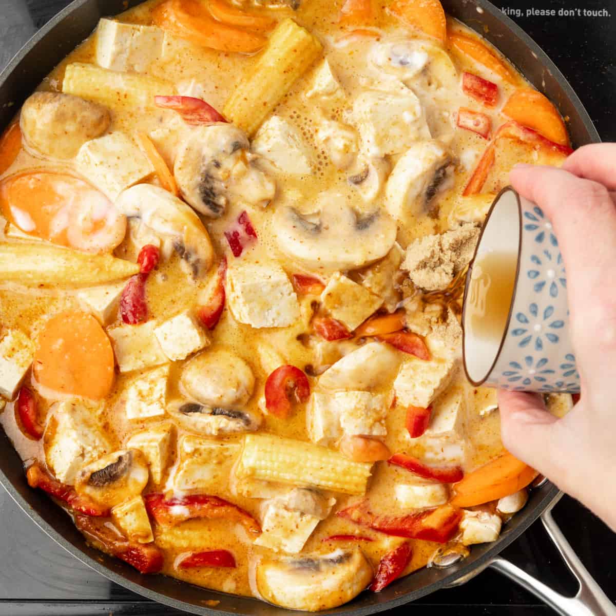 Pouring vegan fish sauce into a pan full of thai red curry.
