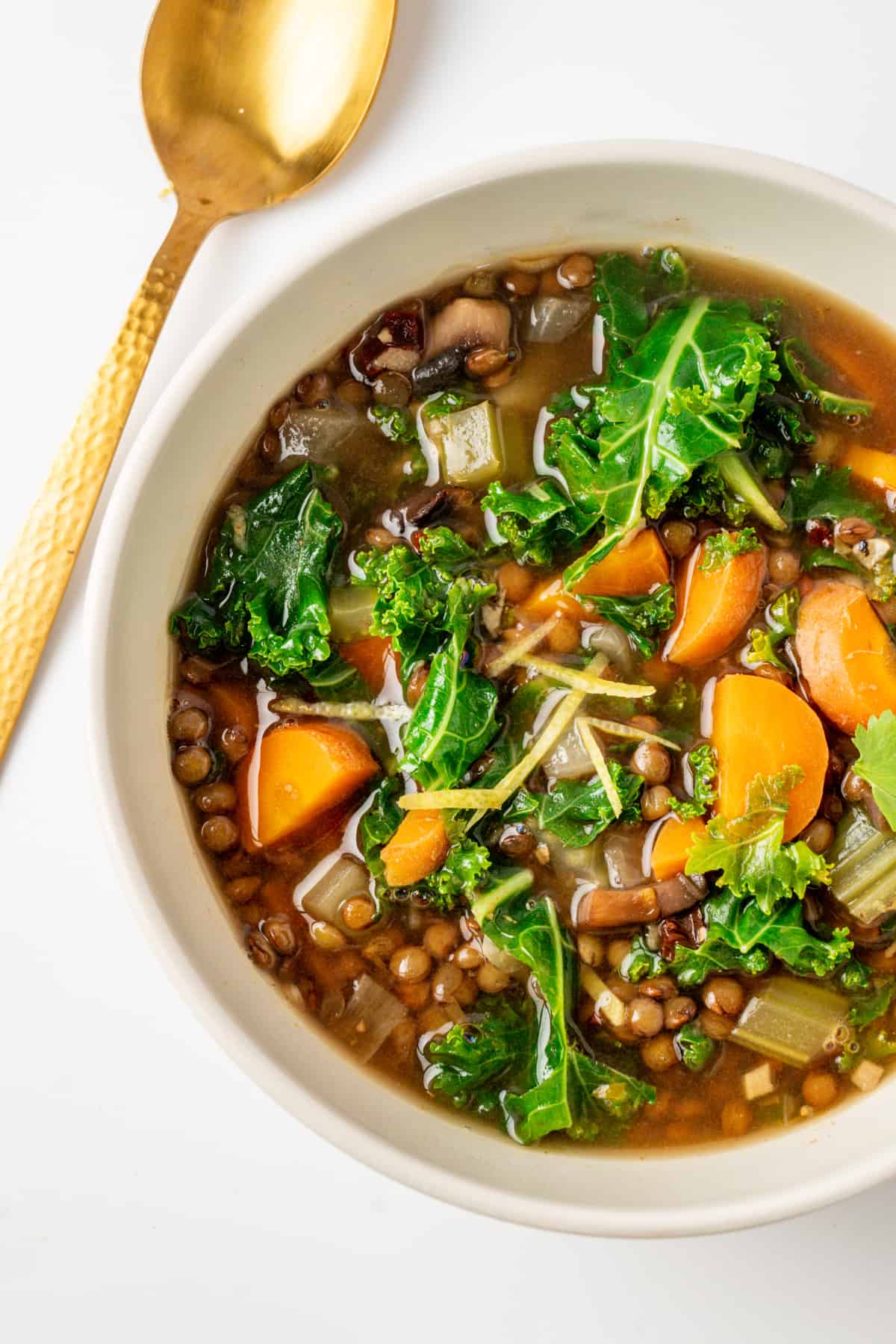 A bowl of soup of lentils with kale with a spoon.