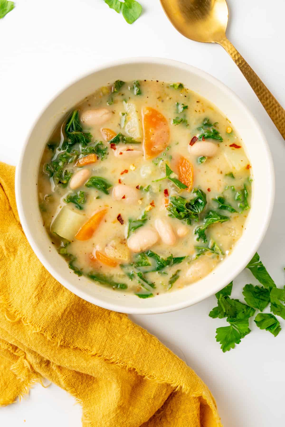 A bowl of white bean soup with pieces of kale, carrot and potato and chili flakes as a garnish.