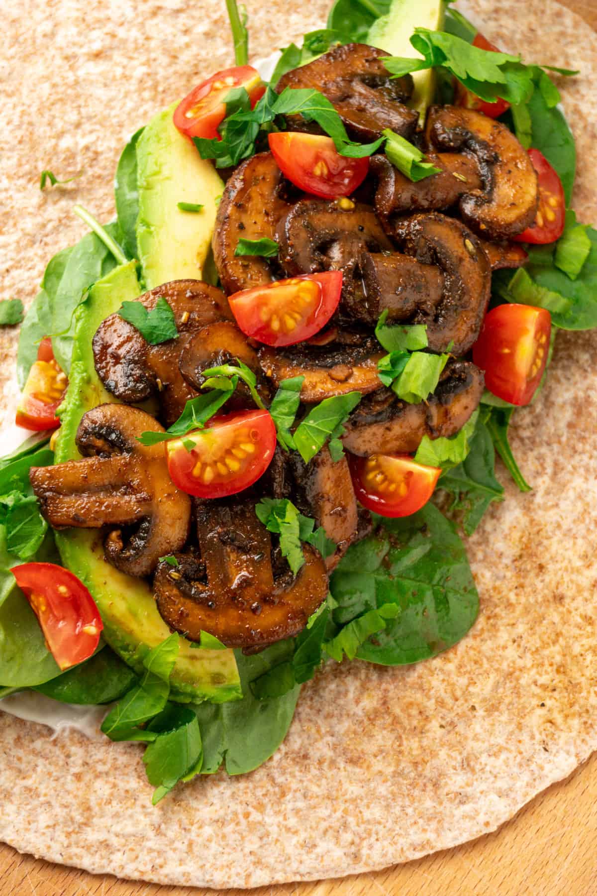 A tortilla wrap topped with mayo, spinach, cherry tomatoes, sauteed mushrooms and chopped parsley.