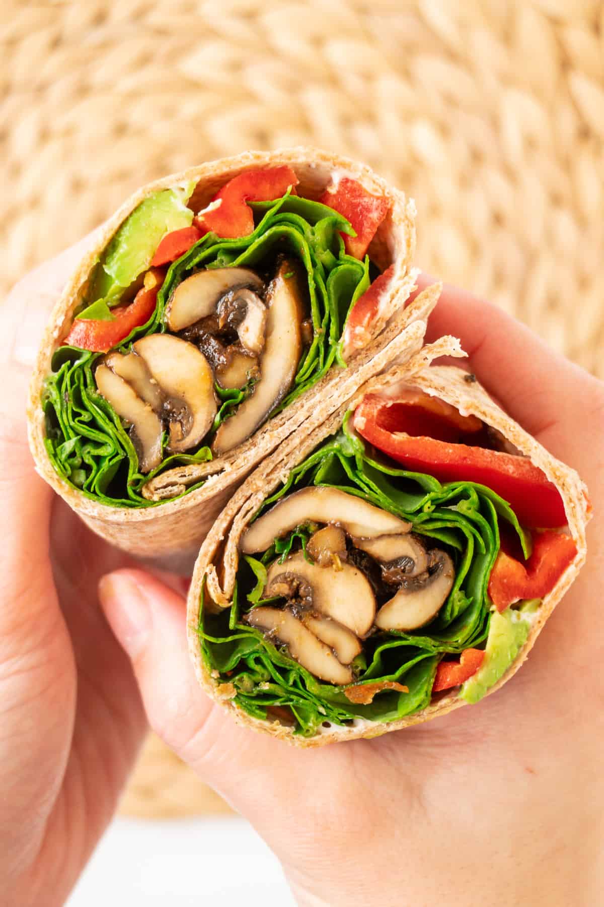 Hands holding a cut open wrap revealing the mushroom, spinach, red pepper and avocado filling.