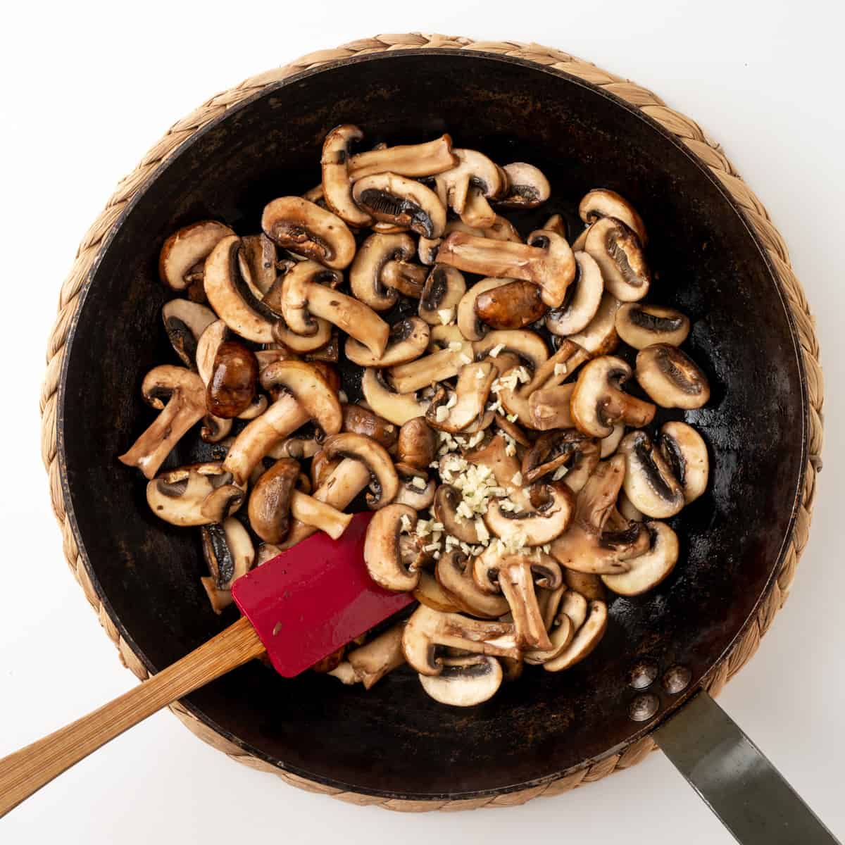 Adding garlic to sliced mushrooms in a skillet.