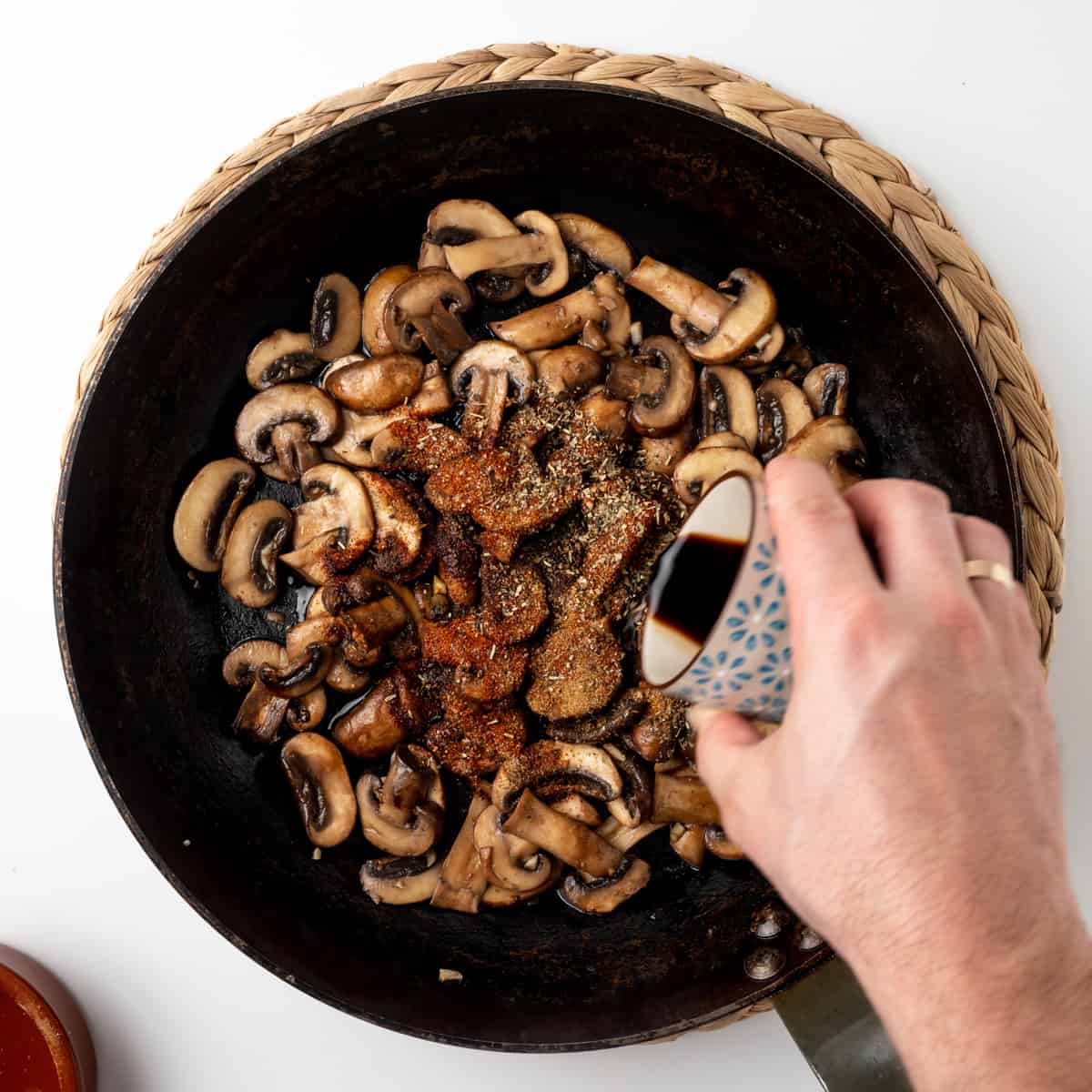 Adding spices, herbs and soy sauce to garlic and mushrooms in a skillet.